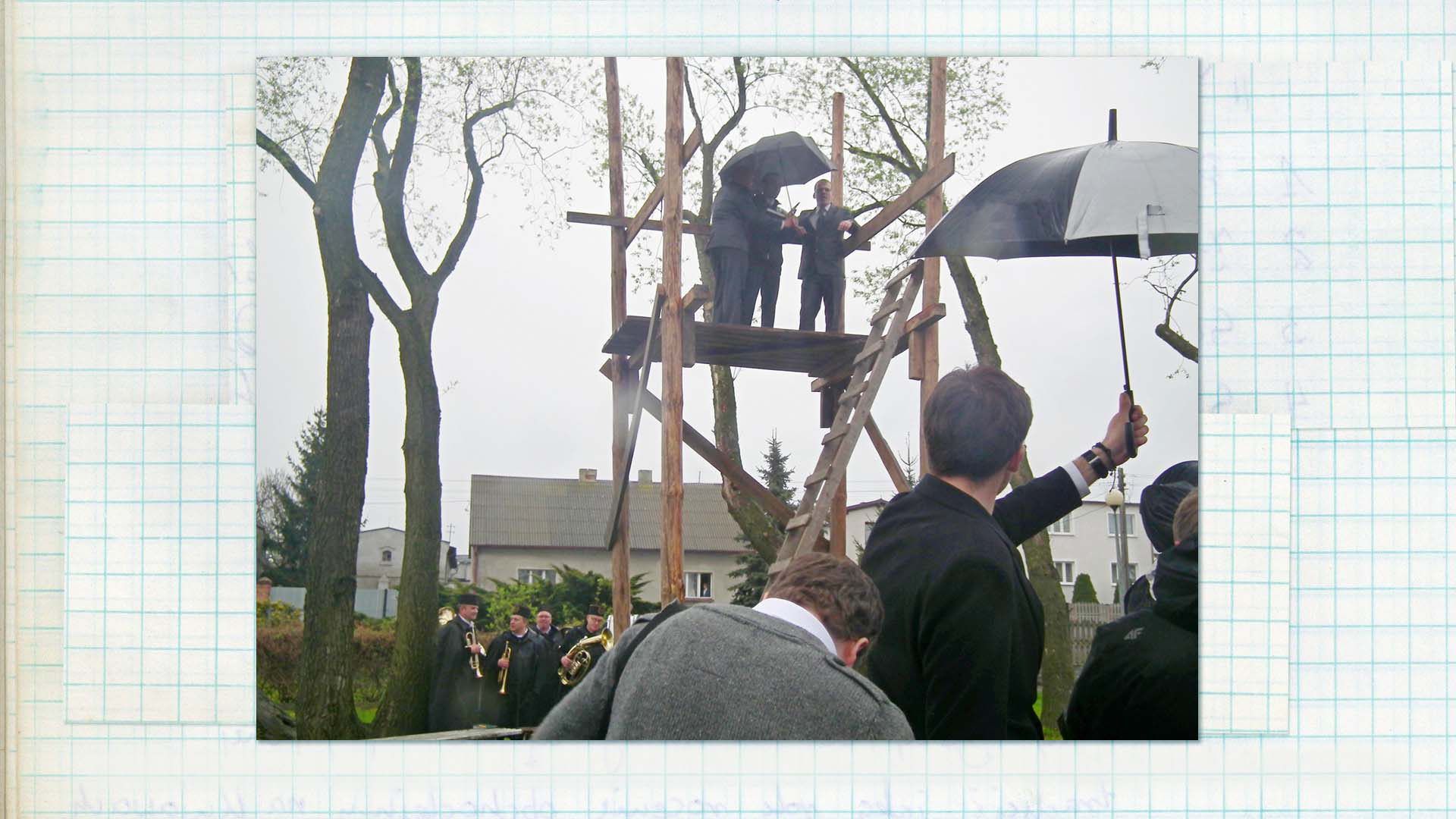 Wygłaszanie przywołówek, Niedziela Wielkanocna, 2014, fot. Paula Kopeć Fotografia w kolorze. Dookoła drewnianej trybuny zgromadziła się publiczność, na jej górze widać stojących pod parasolem trzech mężczyzn.
